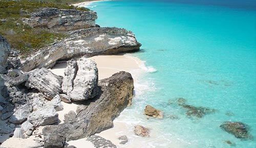 An aerial view of a beach in the Bahamas with turquoise water and rocky cliffs.
