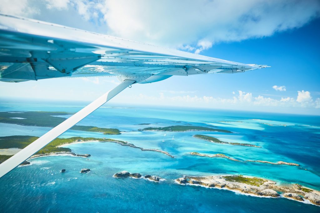 Experience the breathtaking view of a plane wing soaring above the majestic blue ocean while on your all-inclusive vacation to the Bahamas.