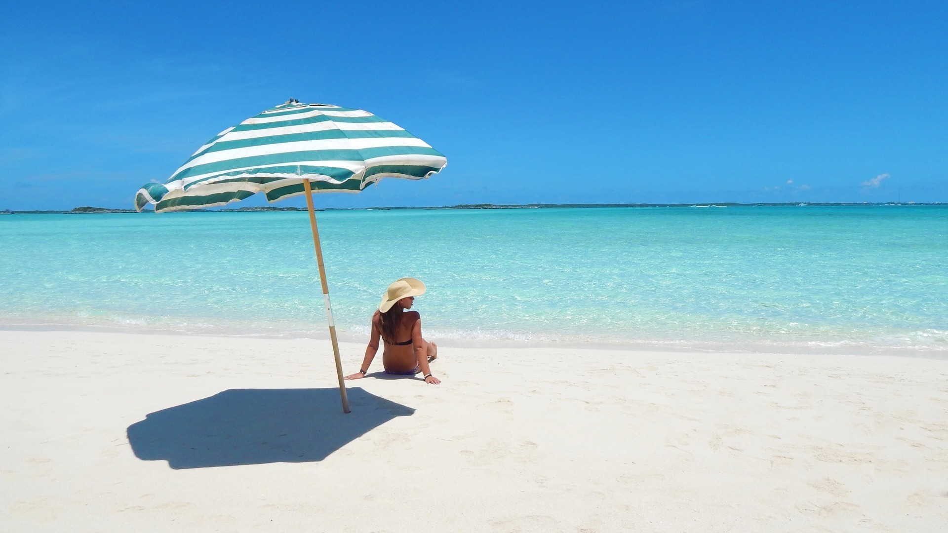 A woman sitting under an umbrella on a sandy beach at Staniel Cay.