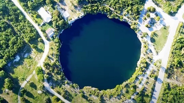 An aerial view of a blue hole in the middle of a forest, part of Bahamas Travel.