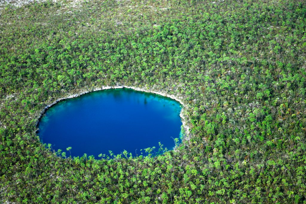 An aerial view of a stunning blue hole nestled in the heart of a lush forest.