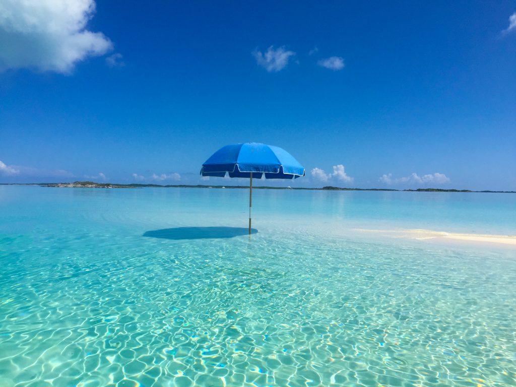 At Staniel Cay, a blue umbrella shades an elegant gathering at the Yacht Club, situated on top of clear blue water.