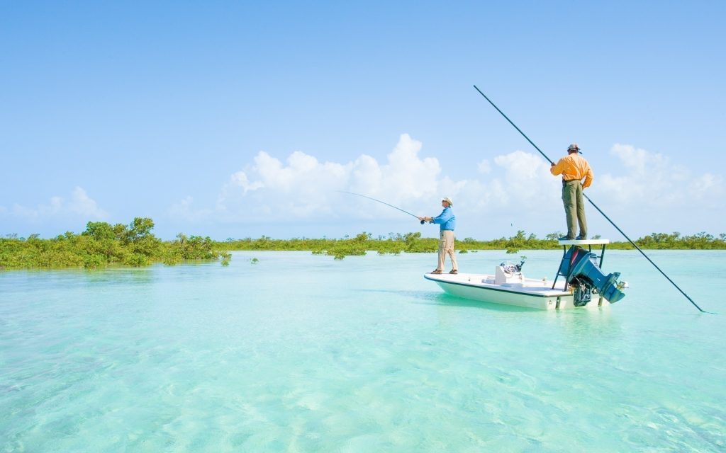 Two men enjoying Bahamas Day tours while fishing on a boat in the clear blue water.