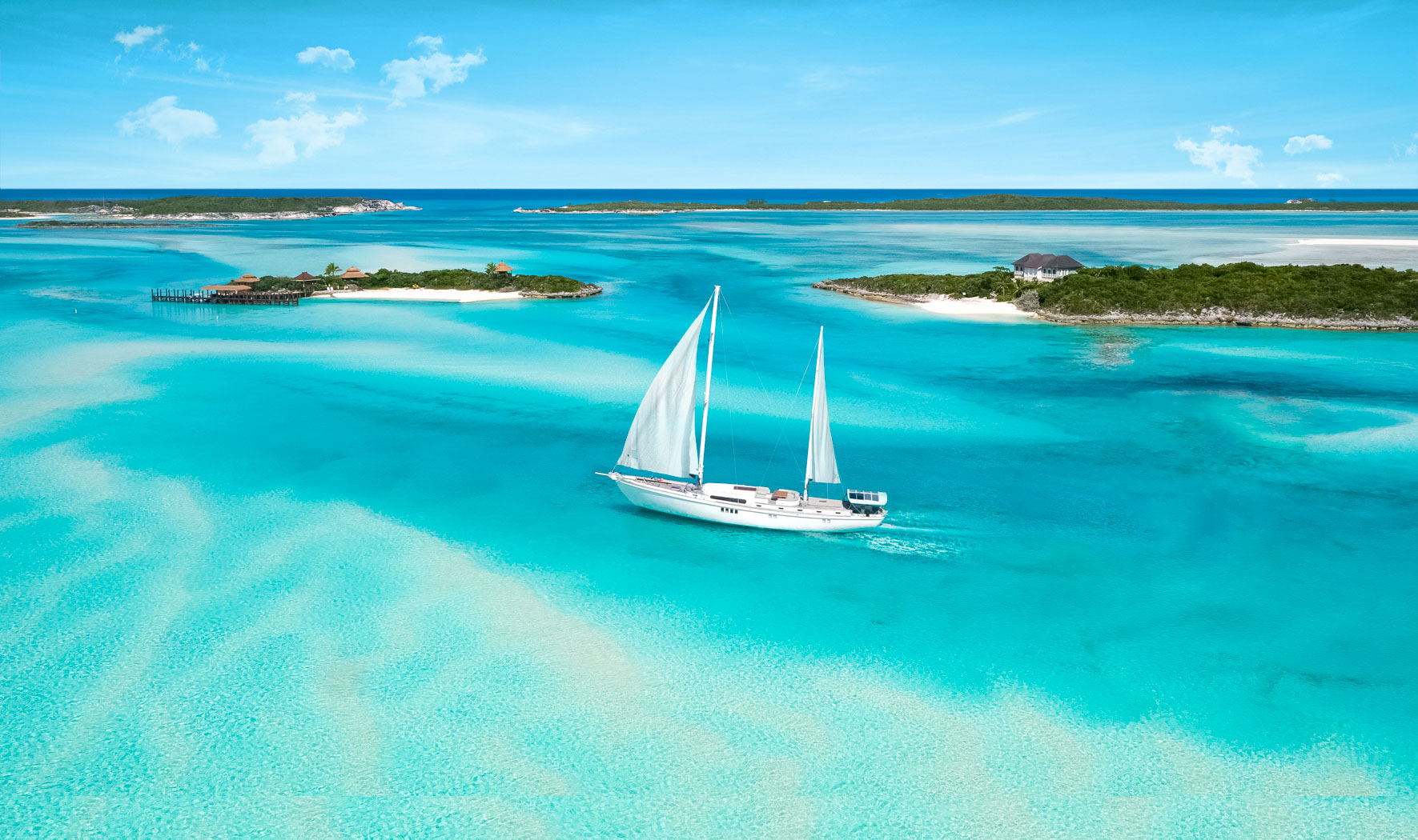 A white sailboat navigates clear turquoise waters near small, lush islands under a blue sky with a few clouds.