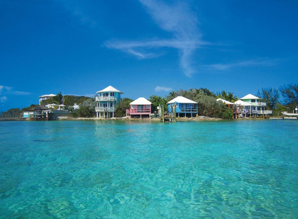 Colorful beach houses on stilts overlook clear turquoise waters under a blue sky near the vibrant Staniel Cay Yacht Club.