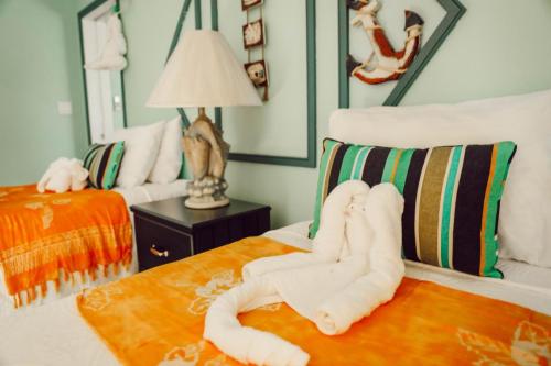 Vacation Rental on Staniel Cay A hotel room with two beds, both decorated with colorful pillows, orange throws, and towel sculptures on top. The wall features nautical-themed decor, including a ship's wheel and anchor.