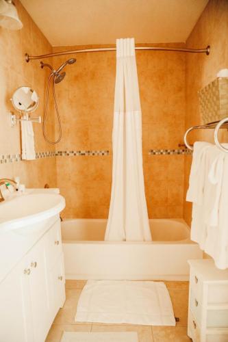 Vacation Rental on Staniel Cay A small bathroom with a white sink, white vanity, bathtub with shower curtain, towels on a rod, a wall-mounted mirror, and a white bath mat on the floor. The walls are tiled in beige.