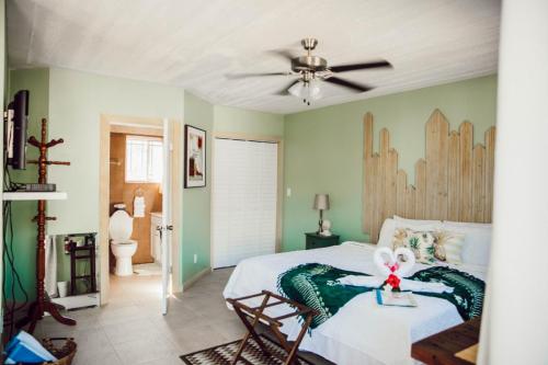A cozy bedroom features a green accent wall, a double bed with white and green bedding, a wooden headboard, a ceiling fan, and an open door leading to a bathroom with a toilet in view.